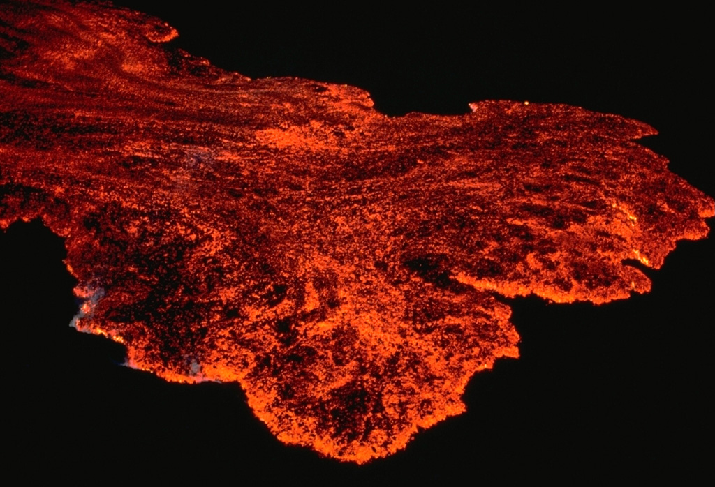 The toe of an April 1984 lava flow advances down the NE rift zone of Mauna Loa volcano in this nighttime view.  The flow margin and much of the surface of the flow is incandescent; darker areas occur where the surface of the advancing lava flow has solidified. Copyrighted photo by Katia and Maurice Krafft, 1984.