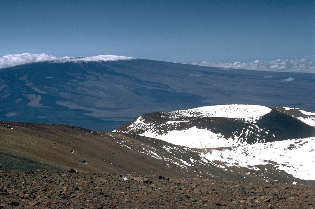 The Pu‘u Haukea scoria cone is one of many recent cones that have formed near the Mauna Kea summit. Mauna Loa is in the background with unvegetated lava flows visible down its flanks. Nearly the entire Mauna Loa surface seen here consists of lava flows erupted during the past 4,000 years. Photo by Lee Siebert, 1987 (Smithsonian Institution).