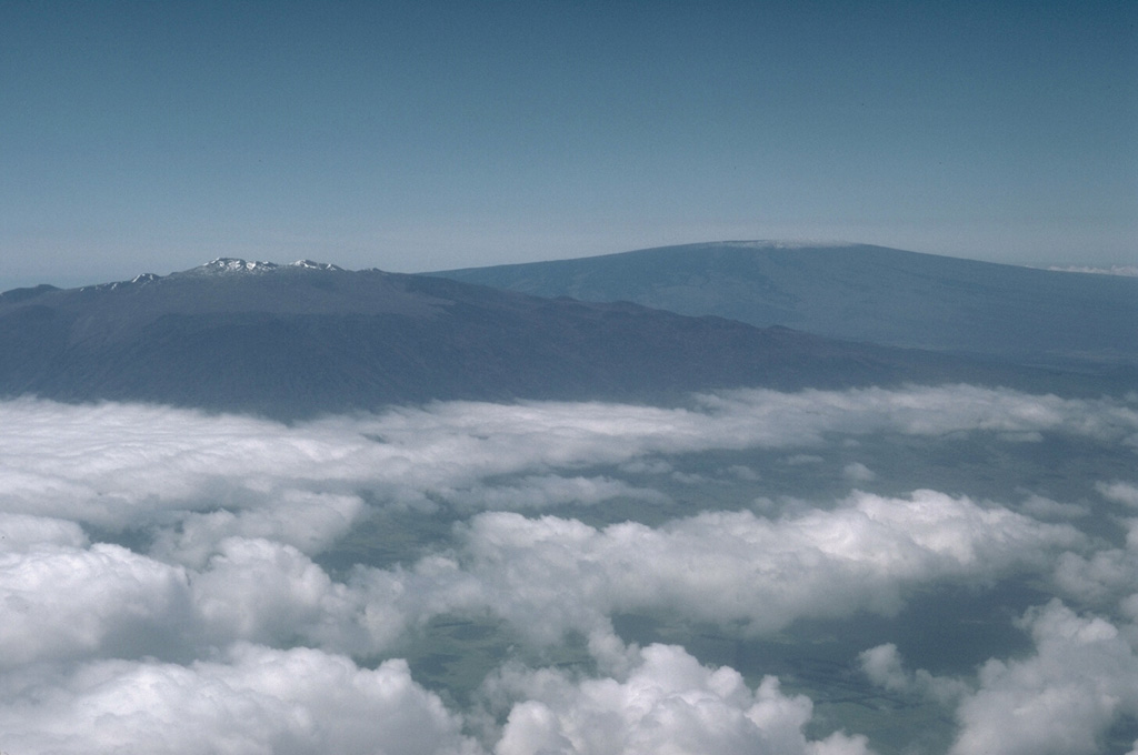 Mauna Kea (left) and Mauna Loa (right), both over 4,000 m above sea level, are also the world's largest active volcanoes, rising nearly 9 km above the sea floor around the island of Hawai’i. This aerial view from the NW shows the contrasting morphologies with the smooth profile of Mauna Loa, and Mauna Kea that was modified by the late-stage products of explosive eruptions. Photo by Lee Siebert, 1987 (Smithsonian Institution).