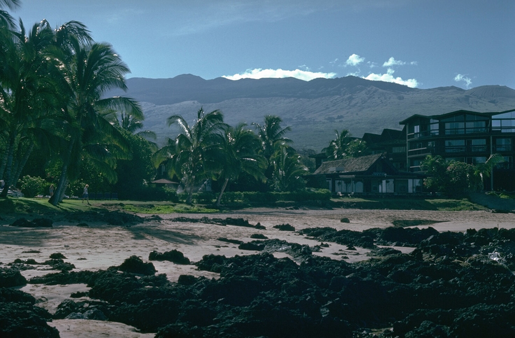 The broad Haleakalā shield volcano towers over the eastern part of the island of Maui, seen here from the beach at Kihei on the west flank. Its summit profile is irregular because of the many scoria cones that have erupted along the SW rift zone, which extends from the coast to the summit. The lava flow in the foreground also originated from Haleakalā.   Photo by Lee Siebert, 1987 (Smithsonian Institution).