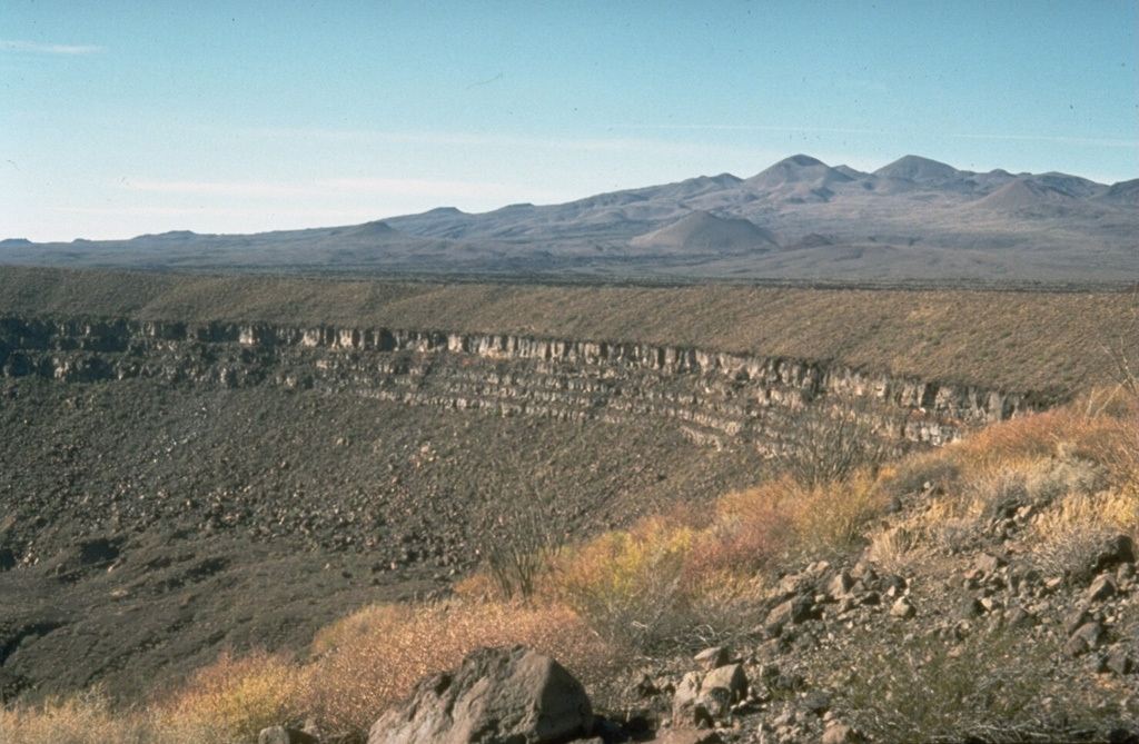 The Pinacate volcanic field covers approximately 55 x 60 km and contains numerous maars and scoria cones. The field is prominent in this arid region of NW México near the head of the Gulf of California. The crater rim across the center of the photo is the 1.6-km-wide Cráter Elegante maar. Pinacate Peak in the distance is at the summit of Santa Clara shield volcano, which contains many scoria cones and lava flow fields. Photo by Richard Waitt, 1988 (U.S. Geological Survey).