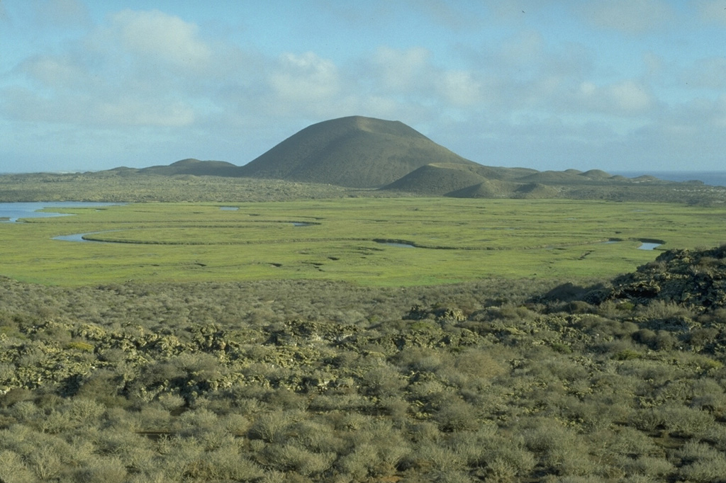 The Volcán Sudoeste scoria cone, and smaller cones at its base, are part of the San Quintín volcanic field in México's Baja Peninsula. They are seen here from the north on the slopes of Picacho Vizcaino. Volcán Sudoeste is one of the youngest scoria cones of the field.  Photo by Jim Luhr, 1990 (Smithsonian Institution).