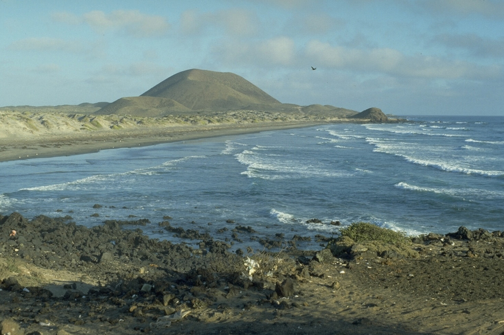Volcán Sudoeste, one of a group of young cones of the San Quintín Volcanic Field, is located at the end of a narrow peninsula extending into the Pacific Ocean. The sand bars along the coast connect Volcán Sudoeste to Monte Mazo, at the southern end of a 10-km-long sand spit. Photo by Jim Luhr, 1990 (Smithsonian Institution).