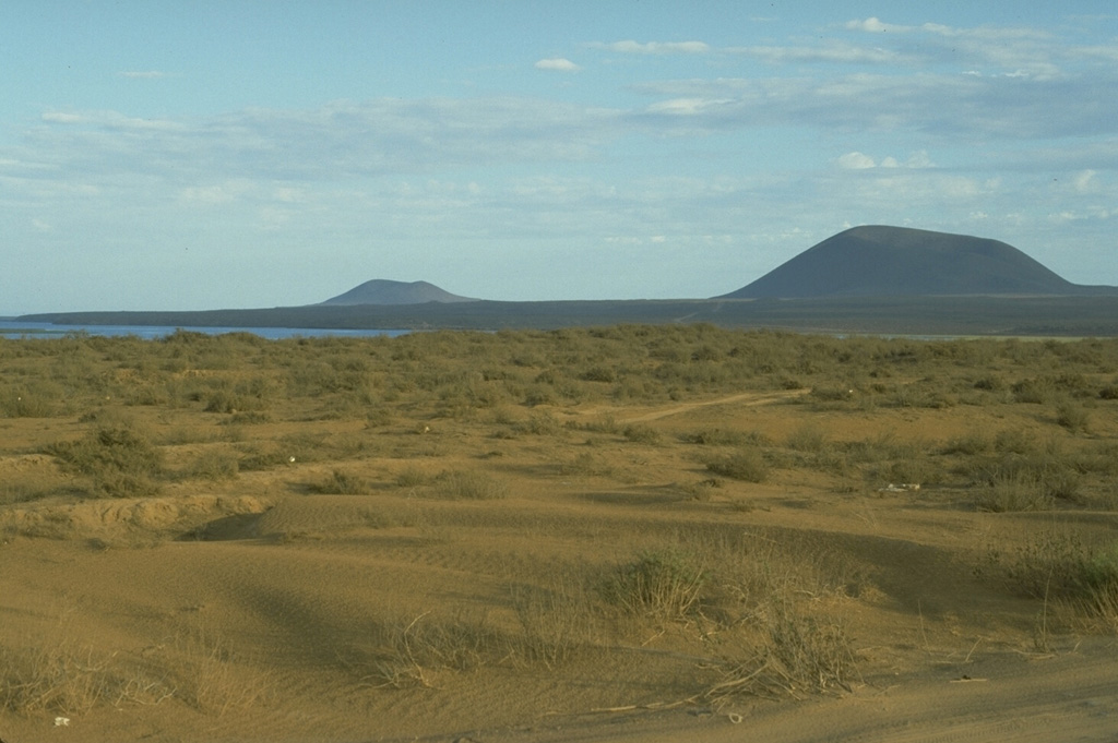 Volcán Ceniza (left) and Cerro Kenton (right), seen here from near Chapala, are two of a group of young scoria cones in the southern part of the San Quintín Volcanic Field in northern Baja California. Along with the Riveroll cone to the NW, they are constructed along a NW-SE trend, one of several fracture patterns in the San Quintín field. The two cones form a peninsula extending into Bahia Falsa, part of which is visible to the left. Photo by Jim Luhr, 1990 (Smithsonian Institution).