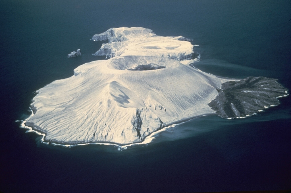Bárcena volcano forms the elongate island of San Benedicto, seen here from the SW in March 1955. The circular summit crater at the center and the lava delta to the right of the tuff cone formed during an eruption in 1952-53. Pleistocene lava domes are located at the far NE tip of the island. Dark-colored lava from the 1952-53 eruption can be seen in the summit crater. Photo by Adrian Richards, 1955 (U.S. Navy Hydrographic Office).