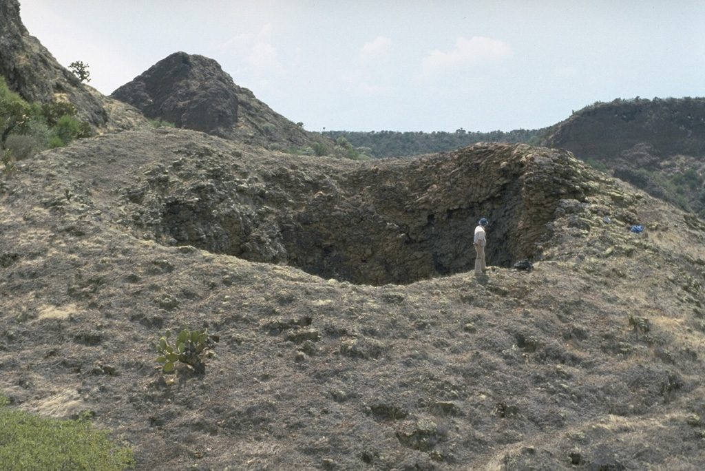 The La Boca crater is a product of the final eruptions of the La Breña-El Jagüey maar complex. La Boca and a nearby small crater, La Boquita, were formed by the accumulation of spatter that welded together during Strombolian activity. The two small craters originated from vents at the SE end of one of the post-maar cones constructed within La Breña maar after the magma-water interaction phase. Photo by Jim Luhr, 1988 (Smithsonian Institution).