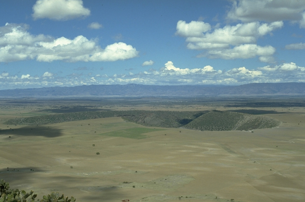 The Durango Volcanic Field covers 2,100 km2 at the eastern edge of the Sierra Madre Occidental (background) of north-central México. The broad lava plain contains about 100 Quaternary scoria cones and several important peridotite and granulite xenolith localities. The La Breña-El Jagüey maar complex, two of the youngest features of the field, are seen here from the ENE at the summit of Cerro Pelón scoria cone.  Photo by Jim Luhr, 1988 (Smithsonian Institution).