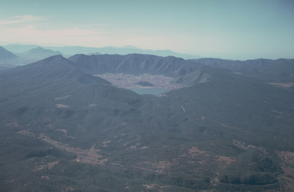 Volcán Tepetiltic is an andesitic and dacitic stratovolcano truncated by an elliptical, 5 x 2.5 km caldera that contains a lake at its NE corner.  The compound caldera, seen here from the NE, was formed during major rhyodacitic eruptions that were closely followed by emplacement of lava domes on the eastern flank.  A permanent caldera lake (center) occupies the lower NE caldera floor.  The small forested lava dome beyond the caldera lake was emplaced near the intersection of the two calderas.   Photo by Jim Luhr, 1978 (Smithsonian Institution).