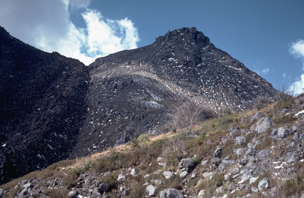 The peak to the upper right is El Volcancito, a lava dome on the NE flank of Colima that began extruding on 12 June 1869 following large explosive eruptions. The dark-colored lava flow with the steep margins to the left erupted from the summit dome during 1975-76. The flow descended the NE flank towards the saddle and then split into two lobes on either side of Volcancito and traveled N and SE. Photo by Jim Luhr, 1987 (Smithsonian Institution).