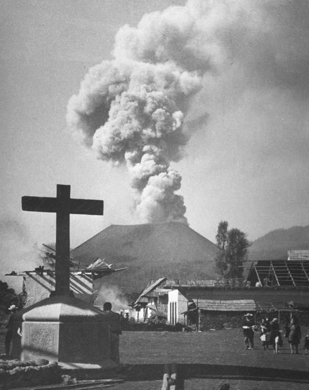 Villagers observe an ash plume rising above Parícutin in 1944 beyond the streets of San Juan Parangaricutiro, soon to be overrun by lava flows. In June and July 1944 lava advanced slowly through the town, which was incrementally evacuated as the flow progressed. Many residents, showing their deep attachment to the land, stayed until the lava overran the last segments of their property. Photo by William Foshag, 1944 (Smithsonian Institution, published in Luhr and Simkin, 1993).