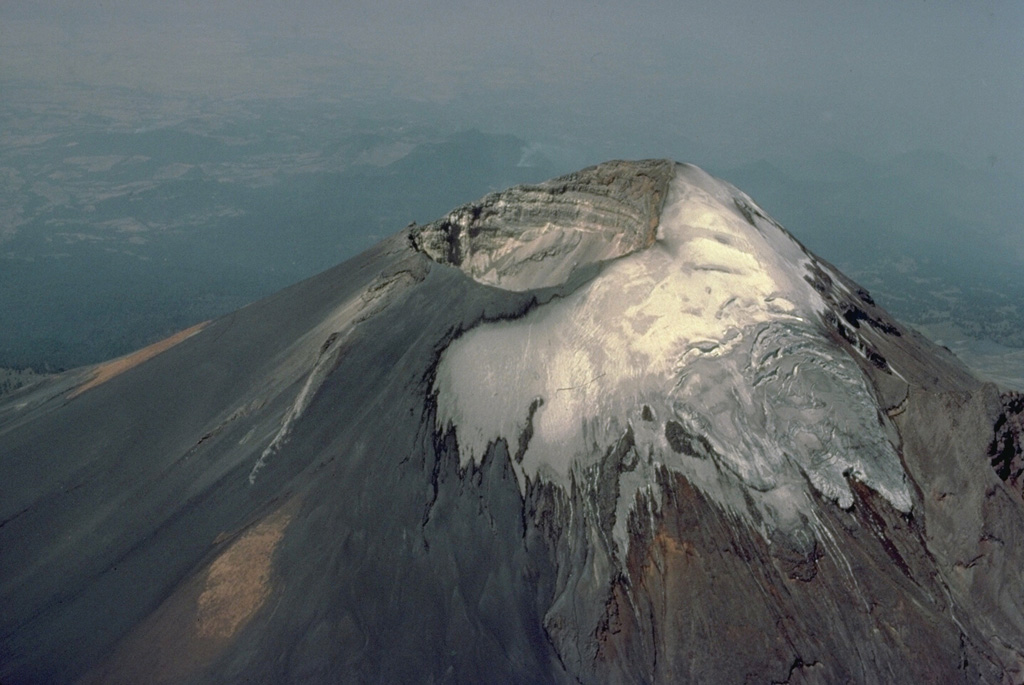 The summit of Popocatépetl volcano, seen here from the north, is cut by a 400 x 600 m wide, steep-walled crater that is elongated in a NE-SW direction.  The crater floor is 500 m below the volcano's summit on the NW rim, which is 170 m above the SE rim.  Historical eruptions of Popocatépetl have originated from this crater and have periodically formed smaller subcraters, pyroclastic cones, or lava domes on its floor. Copyrighted photo by Katia and Maurice Krafft, 1978.