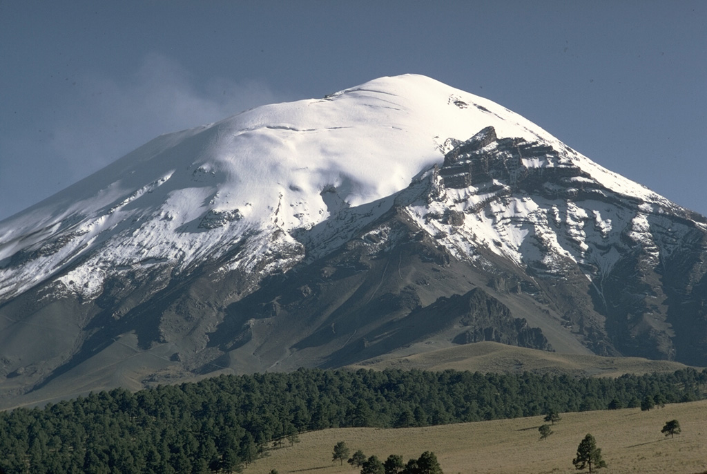 The snow-capped peak of México's Popocatépetl stratovolcano rises above the Tlamacas region to its north. A faint plume rises from a deep summit crater. The sharp peak below the horizon at the right is Ventorrillo, the summit of the eroded Nexpayantla volcano that was a predecessor to Popocatépetl. Its steep cliffs expose the stratified, layered interior of a stratovolcano. Photo by William Melson, 1968 (Smithsonian Institution)