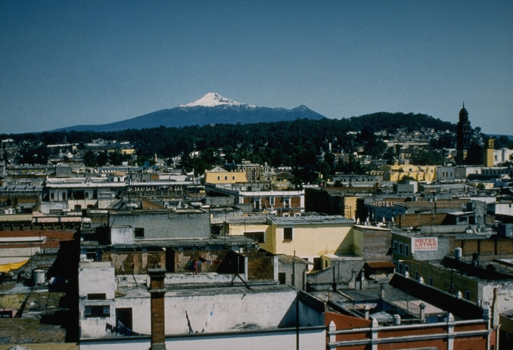The summit of Malinche volcano rises beyond the historical city of Puebla. Pleistocene glaciers have eroded the flanks of the volcano, but at least one of several tuff cones and explosion craters on the flanks is of Holocene age. Photo by Ismael Morales, 1993 (Universidad Autónoma de Puebla).