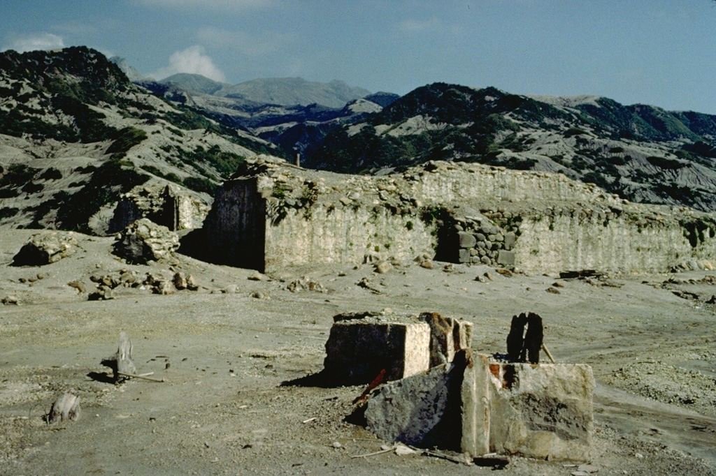 Francisco León was one of 9 villages destroyed by the 1982 eruptions of southern México's El Chichón volcano, seen steaming in the distance in this January 1983 photo.  Powerful laterally moving pyroclastic surges knocked down all walls of buildings in the village, leaving only the basal portion of the massive walls of the village church (center), oriented parallel to their flow.  The village of Francisco León was located 5.5 km SW of the volcano, just within the circular area swept by pyroclastic flows and surges on April 3, the 4th day of the 1982 eruption.   Copyrighted photo by Katia and Maurice Krafft, 1983.