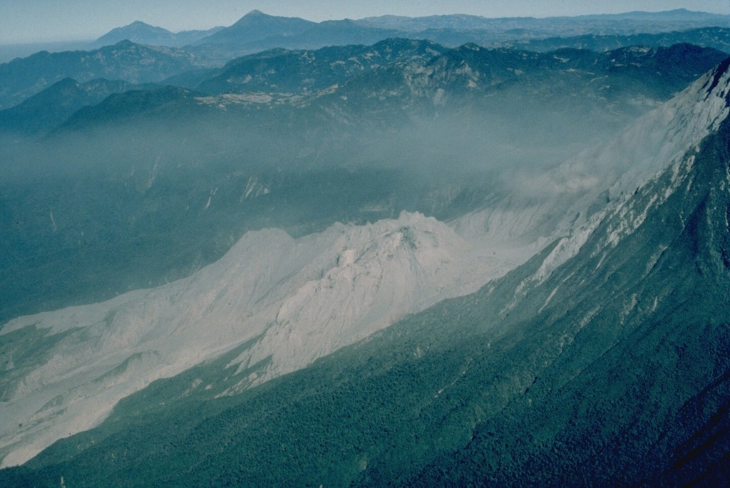 The Santiaguito lava-dome complex (center) has been in continual activity since 1922.  It is seen here in March 1983 from the SE, with Siete Orejas volcano forming the broad forested ridge above it and Tacaná (left) and Tajumulco (right) volcanoes appearing on the left skyline.  Santiaguito was constructed within the large 1902 explosion crater, which cuts the SW flank of Santa María volcano at the right. Copyrighted photo by Katia and Maurice Krafft, 1983.