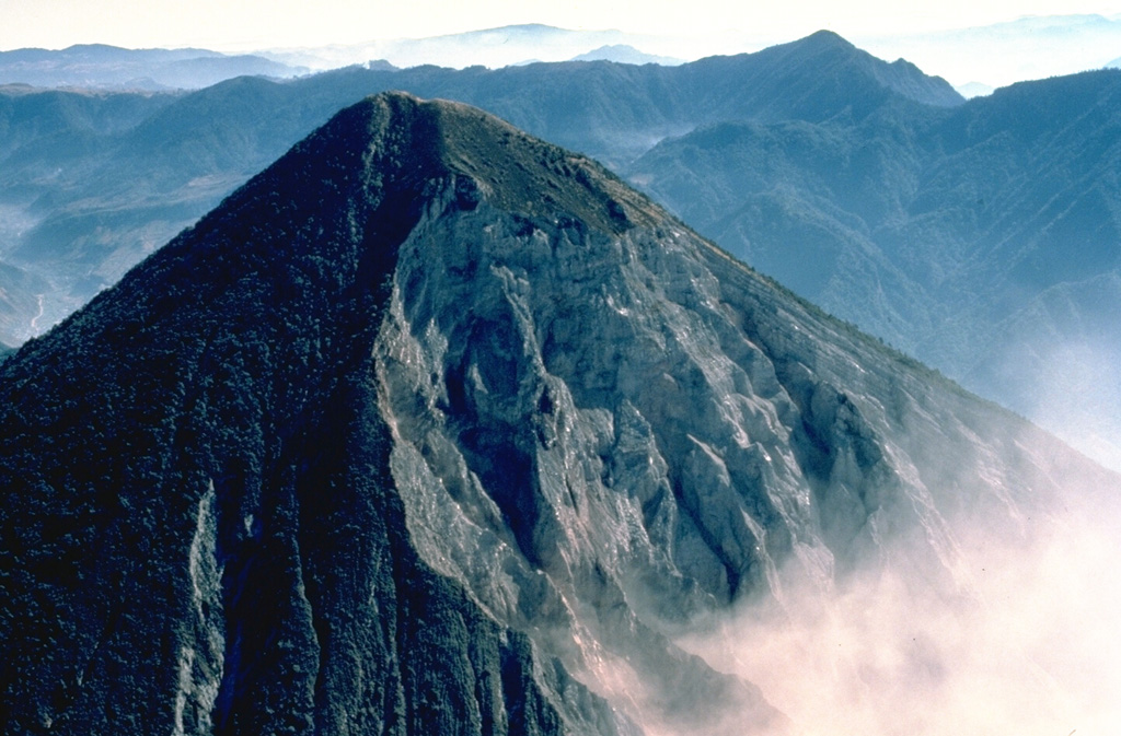 The SW flank of 3772-m-high Santa María volcano, seen here from the west in March 1983, is cut on the right by a large crater produced during an eruption in 1902.  The upper rim of the 1-km-wide crater extends to just below the summit.  The diffuse smoke plume at the lower right is the remnant of an explosive plume from Santiaguito lava dome, which has been growing since 1922 at the base of the 1902 crater. Copyrighted photo by Katia and Maurice Krafft, 1983.