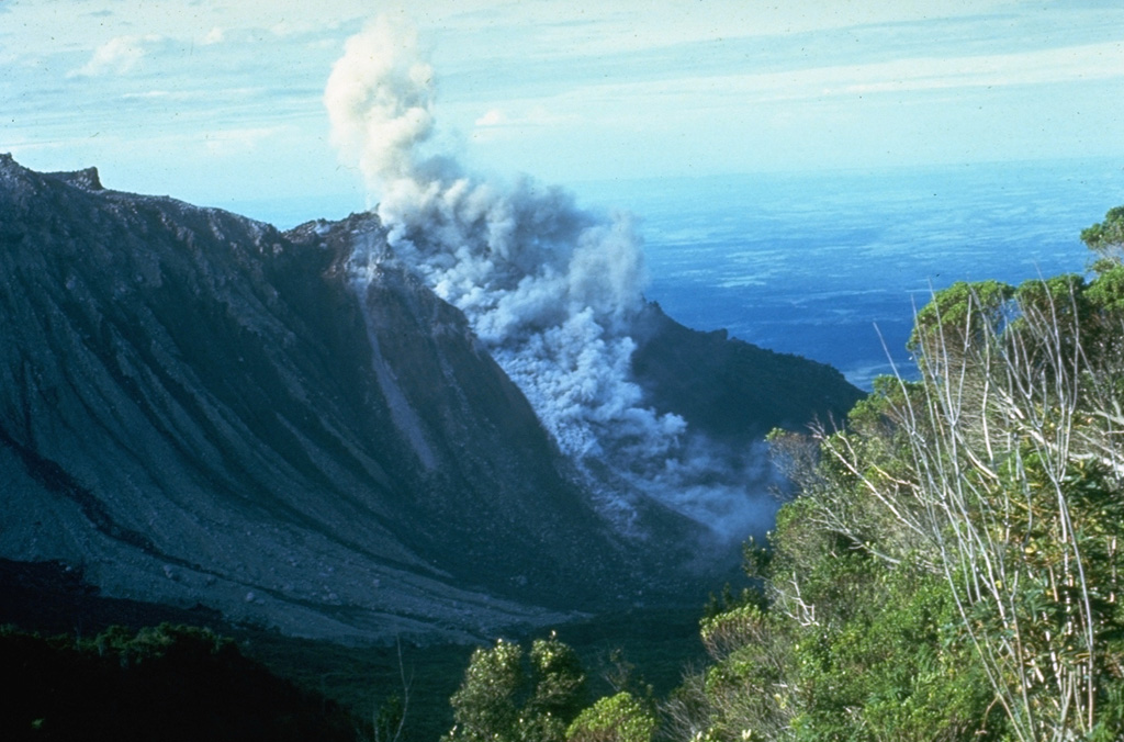 A small block-and-ash flow produced by a small collapse of the growing lava dome descends about 750 m down the north flank of El Brujo dome on 7 July 1967. The Pacific coastal plain is visible in the distance. El Brujo was the westernmost dome of the compound Santiaguito lava dome, which extends about 3 km in a roughly E-W direction. Photo by Dick Stoiber, 1967 (Dartmouth College).