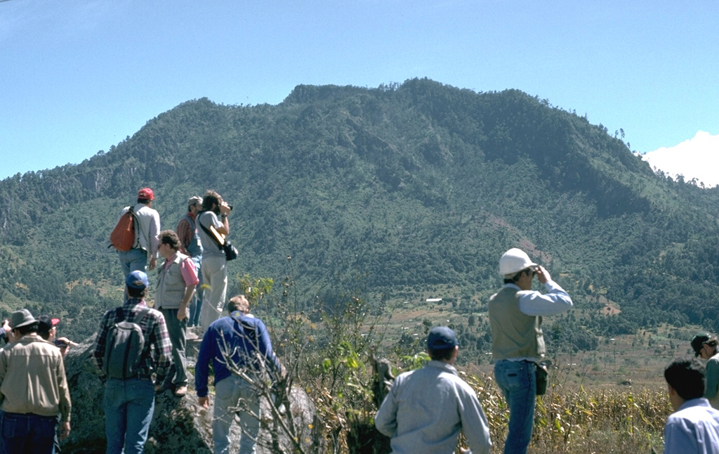 A group of volcanologists are standing on the surface of a debris avalanche deposit produced by collapse of the Cerro Quemado NE flank about 1,150 years ago, with the avalanche scarp in the background to the SW. The scarp, which fills all but the far right-hand slope of this view, is 1 x 1.5 km wide. An associated lateral blast also swept across a 40 km2 area to the NE. The eruption concluded with the emplacement of a small lava dome near the headwall of the scarp. Photo by Lee Siebert, 1993 (Smithsonian Institution).