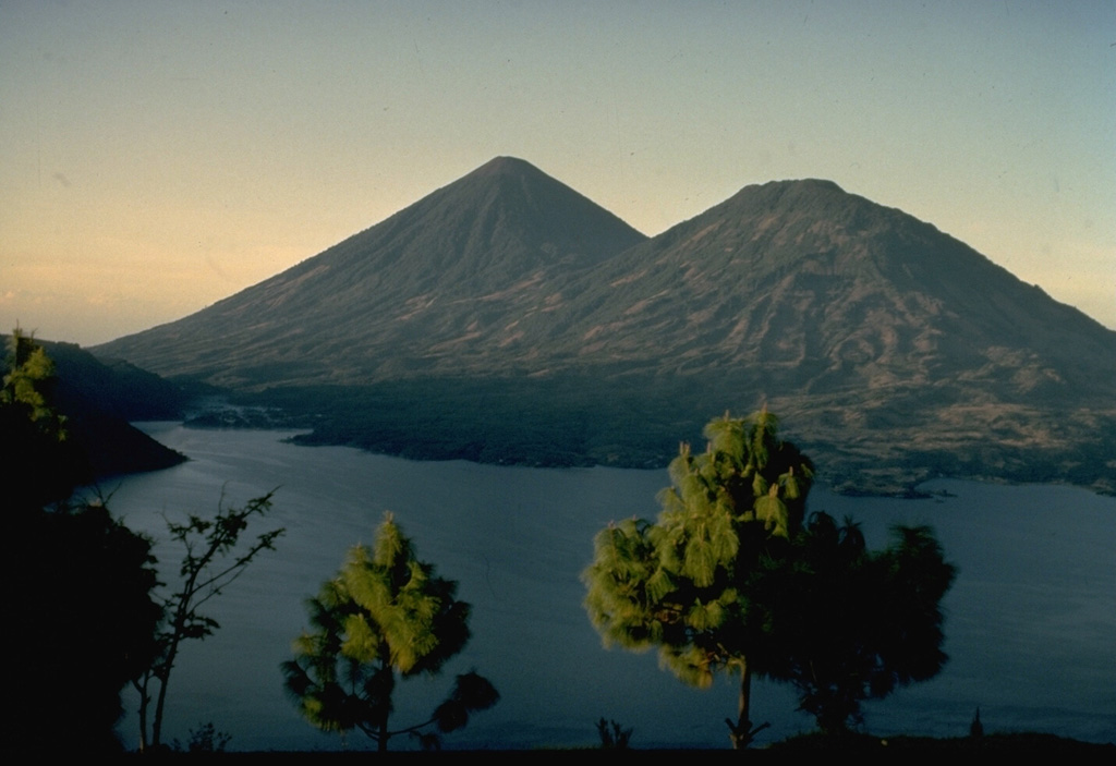 Atitlán (left) and Tolimán (right) are twin stratovolcanoes on the shores of Lake Atitlán, one of the scenic highlights of Guatemala.  The historically active Atitlán is younger than Tolimán, although their activity overlaps.  The surface of Tolimán is draped by prominent thick lava flows, in contrast to the extensive pyroclastic cover on Atitlán.  Tolimán lava flows, erupted from both summit and flank vents, have produced a pronounced embayment with an irregular shoreline that extends into the lake.  This view is from the NE on the rim of Atitlán caldera. Copyrighted photo by Katia and Maurice Krafft, 1974.