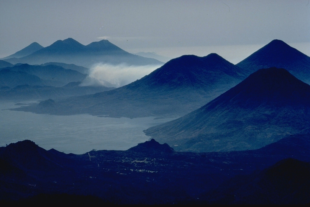 This dramatic photo looking SE down the axis of a chain of volcanoes extending across Guatemala shows six Quaternary volcanoes and one large caldera.  Beginning in the right foreground are three volcanoes, San Pedro, the conical Atitlán, and Tolimán, that are constructed on the southern shore of Lake Atitlán, which fills a large Pleistocene caldera.  The three volcanoes in the distance are, from left to right, Agua, Acatenango, and Fuego.  Tolimán-Atitlán and Acatenango-Fuego are paired volcanoes along N-S lines. Copyrighted photo by Katia and Maurice Krafft, 1983.