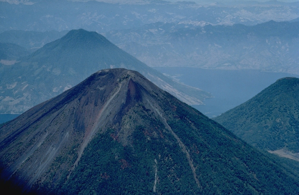 Volcán Atitlán, seen here from the SE with San Pedro volcano behind it and Tolimán volcano to its left, is a conical stratovolcano that rises to 3535 m south of Lake Atitlán (right).  The historically active Atitlán is younger than Tolimán, although their activity overlaps.  The northern side of the volcano is wooded to near the summit, whereas the upper 1000 m of the southern slopes, seen here, are unvegetated.  Predominatley explosive eruptions have been recorded from Volcán Atitlán since the 15th century. Copyrighted photo by Katia and Maurice Krafft, 1983.