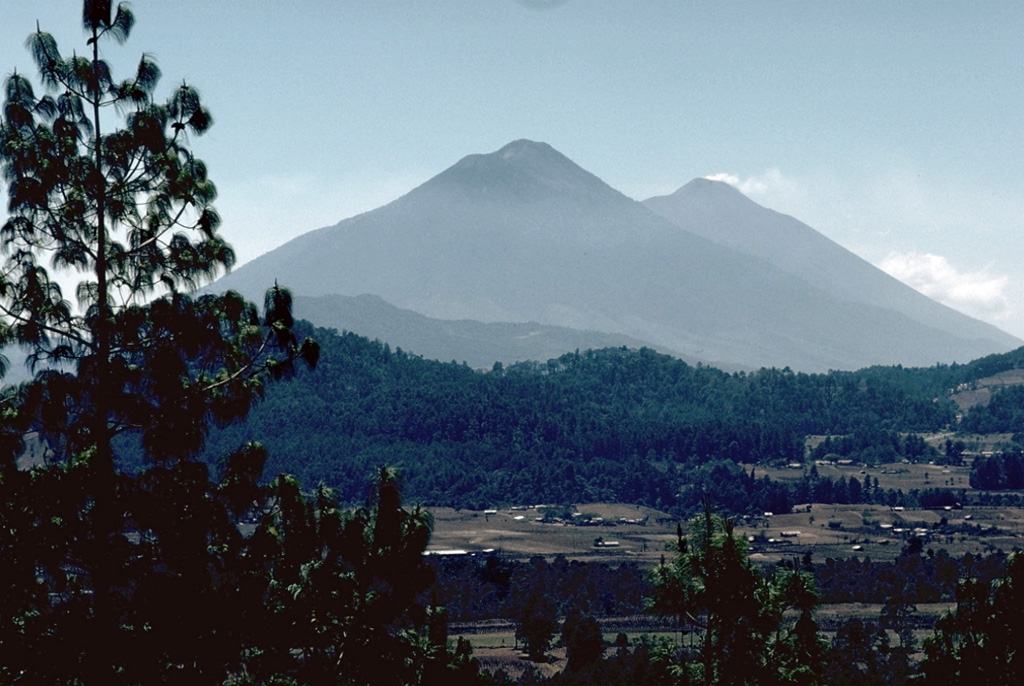 The Acatenango-Fuego complex is seen here from the NW. A gas plume drifts from the summit of Fuego (right), beyond Acatenango (center). Like other N-S-trending volcanic chains in the Guatemalan highlands, activity at the Acatenango-Fuego chain migrated to the south. Yepocapa, the northernmost summit of Acatenango, was active from about 70,000 to 20,000 years ago, after which Acatenango's northern Pico Mayor was constructed. The frequently active Fuego volcano formed during the Holocene. Photo by Lee Siebert, 1988 (Smithsonian Institution).