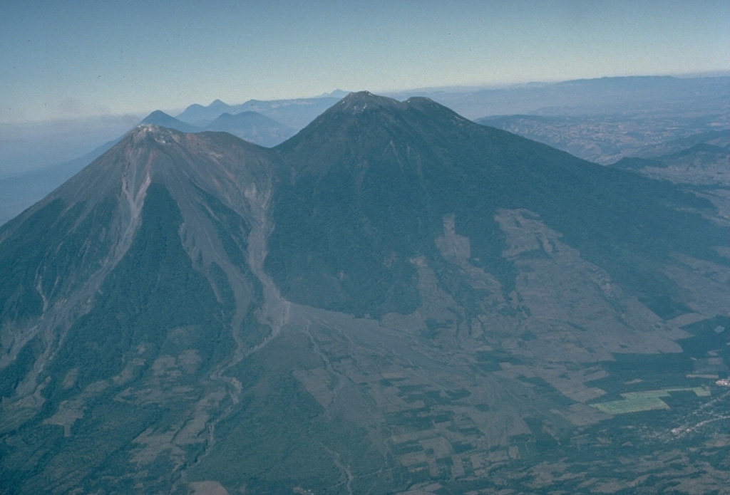 The paired volcanoes of Fuego (left) and Acatenango, seen here in profile from the ESE, illustrate the N-S progression of volcanism that is typical of paired volcanoes in Guatemala and México.  Activity at Yepocapa (right), the lower northern summit of Acatenango, ended about 20,000 years ago, after which Acatenango's highest cone, Pico Mayor, was built.  Activity then again migrated southward to build Meseta volcano, a remnant of which forms the shoulder left of the saddle between Acatenango and Fuego.  Lastly, modern Fuego was constructed south of Meseta volcano. Copyrighted photo by Katia and Maurice Krafft, 1983.