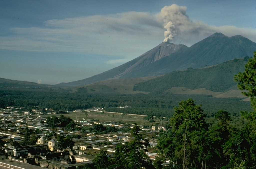 An ash column rises above the summit of Fuego volcano in early December 1974 with the city of Antigua in the foreground.  This relatively minor activity took place near the end of one of Fuego's largest historical eruptions, which began in October.  The twin summits of Acatenango, Pico Mayer (right) and Yepocapa (left), appear at the upper right. Copyrighted photo by Katia and Maurice Krafft, 1974.