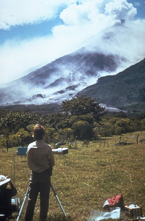 Scientists use a COSPEC (Correlation Spectrometer) instrument to measure the sulfur dioxide (SO2) content of a volcanic plume from Fuego volcano in Guatemala. Measuring the amount of SO2 and other gases in volcanic plumes are useful tools for eruption monitoring. This photo of Dick Stoiber (left) and Gary Malone (standing) was taken by Tom Crafford from Finca Capetillo NE of Fuego during its October 1974 eruption. Photo by Tom Crafford, 1974 (Dartmouth College, courtesy of Dick Stoiber).
