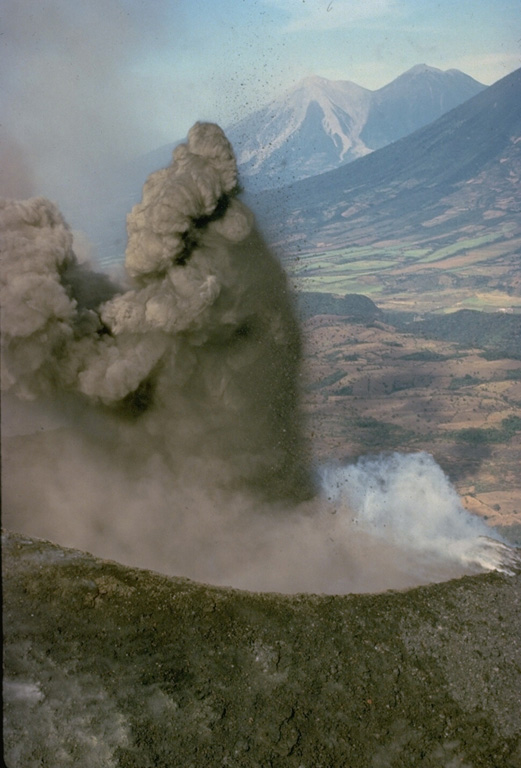 An explosion from MacKenney crater on Pacaya volcano ejects a dark, ash-rich column and individual blocks that are sometimes incandescent even during daylight hours.  This December 1974 photo shows Fuego (left) and Acatenango (right) volcanoes in the background, behind the sloping flanks of Agua volcano. Copyrighted photo by Katia and Maurice Krafft, 1974.