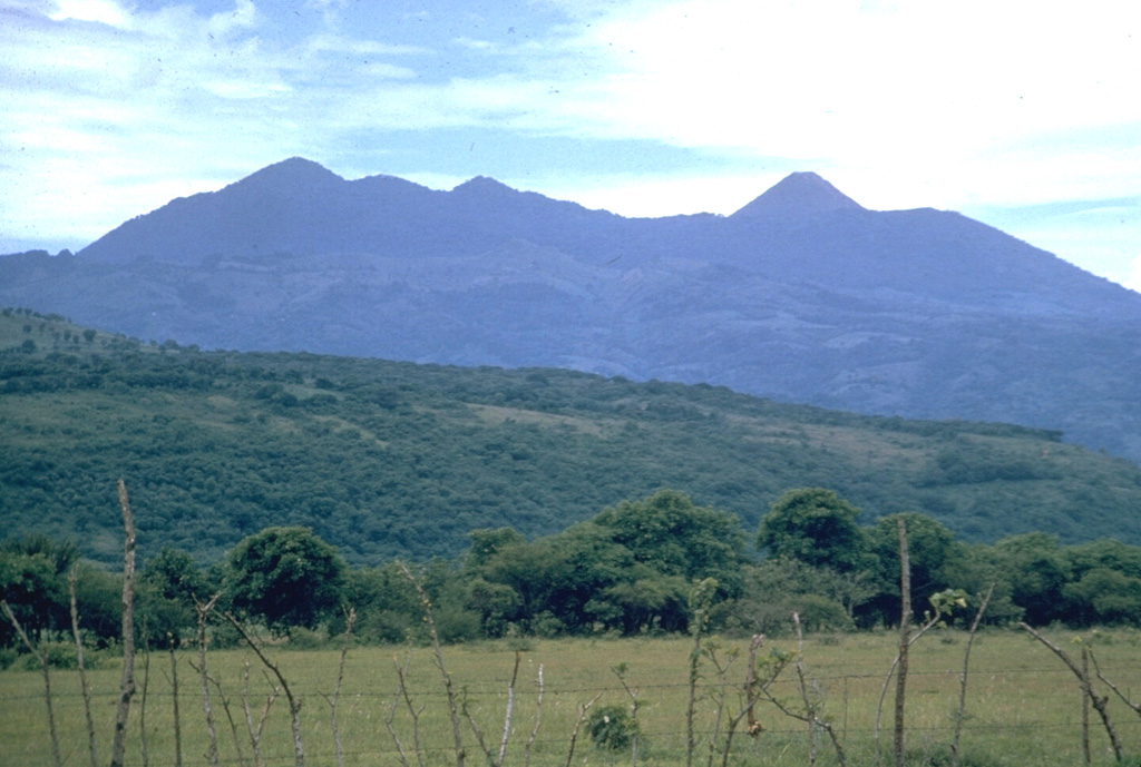 The Pacaya volcanic complex is seen here from the north. The rounded Cerro Grande lava dome forms the high point to the left. The peak to the right is the historically active cone of Pacaya. It was constructed within an arcuate crater whose rim forms the flat ridge on either side of the cone. This September 1962 photo was taken prior to a long-term eruption beginning in 1965 from a new vent on the western flank. Frequent eruptions built MacKenney cone, which grew to the height of the previous cone. Photo by Dick Stoiber, 1962 (Dartmouth College).