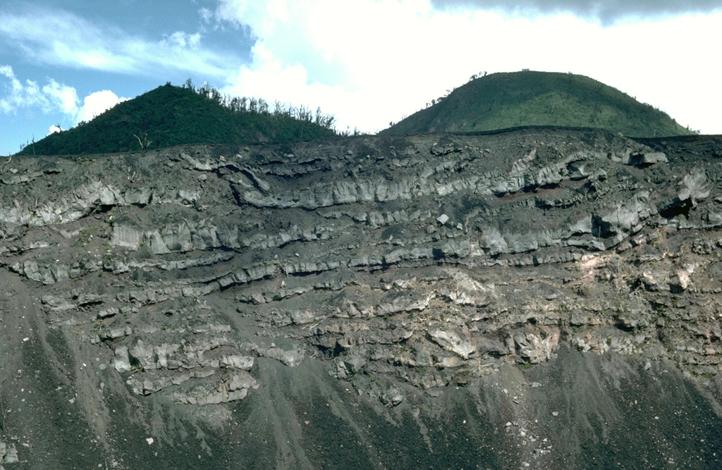 A sequence of thin lava flows forms the upper part of the Pacaya NE crater wall. These basaltic lava flows were erupted during the final stages of an ancestral Pacaya edifice, which collapsed sometime between about 1,550 and 600 years ago to form a large horseshoe-shaped crater. The upper approximately 50 m of the wall is seen in this view with Cerro Grande, an older dome of Pacaya, forming the rounded peak to the right with the Cerro Chiquito cone to the left. Photo by Lee Siebert, 1988 (Smithsonian Institution).