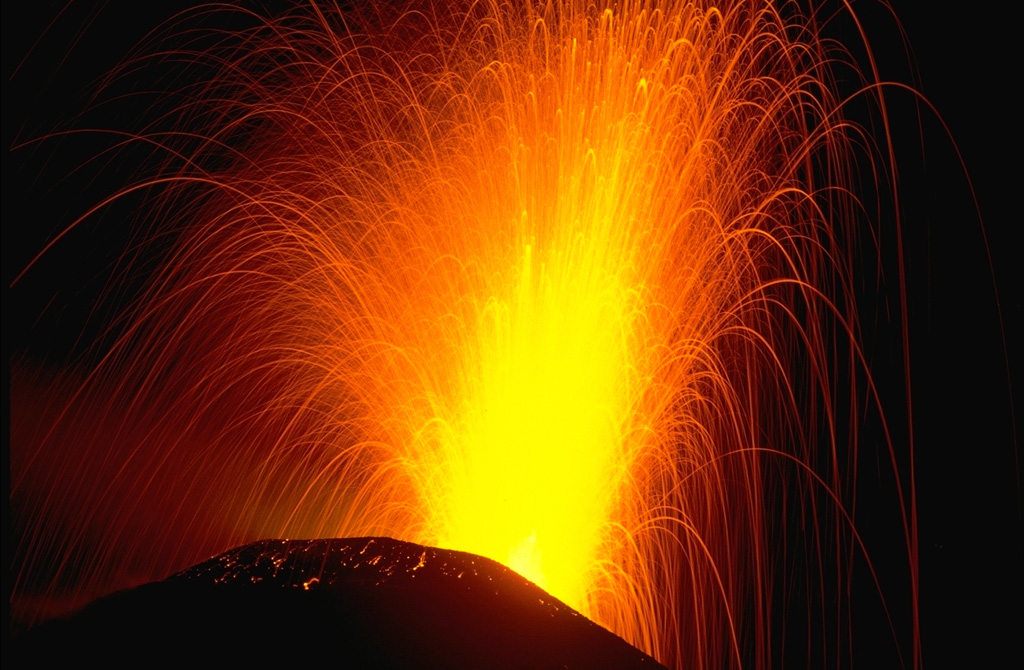 Strombolian explosions such as this one in November 1988 are typical at Pacaya. The ballistic traces of individual volcanic bombs that incrementally build MacKenney cone are seen in this time exposure. Cyclical activity lasting for several decades has consisted of long-term moderate explosive eruptions accompanied by periodic lava effusion that builds up the cone. This long-term moderate activity is punctuated by more infrequent larger explosions that destroy the upper part of the cone, after which the cone is reconstructed. Photo by Lee Siebert, 1988 (Smithsonian Institution).