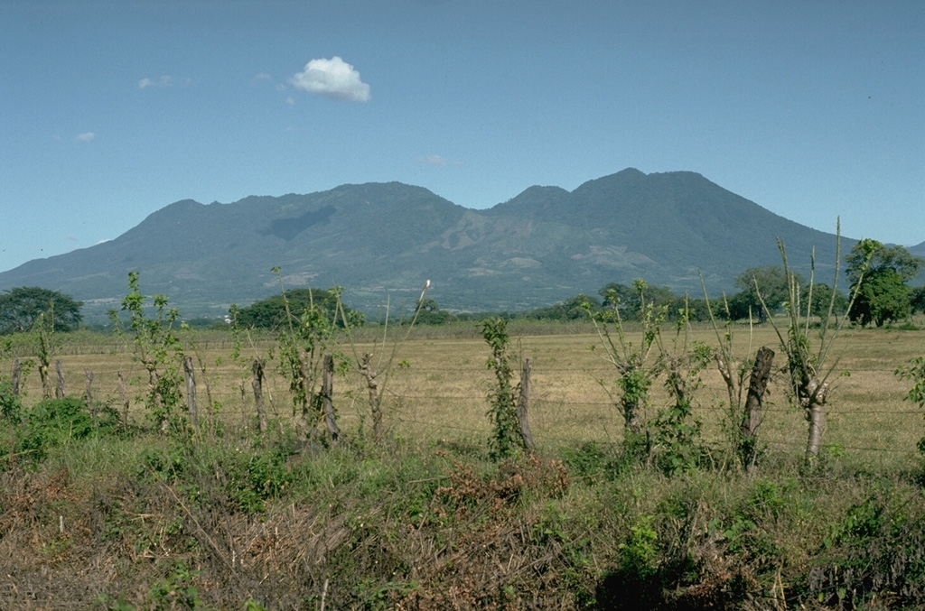 Tecuamburro, seen here from the SE on the Pacific coastal plain, is a small lava-dome complex of mostly Pleistocene age. Tecuamburro and other lava domes forming the right-hand peaks were constructed during the late Pleistocene or early Holocene within a horseshoe-shaped, east-facing crater. The crater resulted from structural failure of the older Miraflores stratovolcano on the left.  Photo by Lee Siebert, 1988 (Smithsonian Institution).