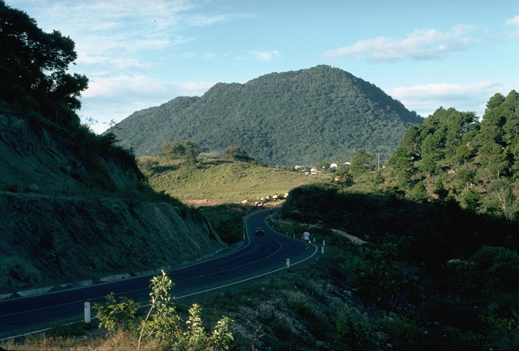 This view from the south shows a forested lava dome, one of a cluster of at least three coalescing domes that form the summit of Moyuta. The town of Moyuta, the outskirts of which are seen in the center of the photo, is located high on the volcano immediately adjacent to the summit dome complex. Photo by Lee Siebert, 1988 (Smithsonian Institution).