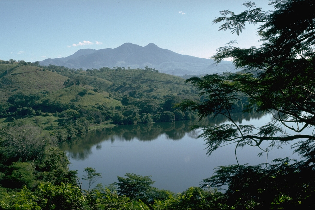 Moyuta is the easternmost of a chain of large volcanoes extending along the volcanic front of Guatemala. The summit contains a cluster of forested lava domes. It is viewed here from a small lake to its SW at the edge of the Pacific coastal plain.  Photo by Lee Siebert, 1988 (Smithsonian Institution).