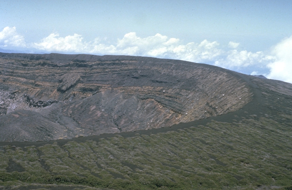 The broad summit of Santa Ana volcano has a 1.5-km-wide crater seen here from the south. The series of bedded phreatomagmatic tephra layers exposed in the crater wall in this photo form the summit region and overlie lava flows exposed lower in the crater walls. Photo by Dick Stoiber, 1966 (Dartmouth College).