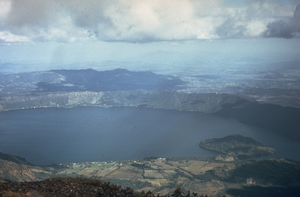 Coatepeque caldera iseast of Santa Ana volcano. The eastern caldera rim rises about 250 m above the lake surface in this 1972 photo. Post-caldera eruptions included the formation of basaltic scoria cones and flows near the western margin, and the extrusion of lava domes (such as Cerro Grande forming the island to the right) along a NE-SW line near the caldera lake margins.  Photo by Dianne Neilson, 1972 (courtesy of Dick Stoiber, Dartmouth College).