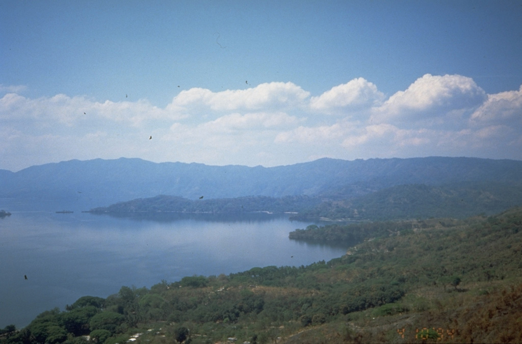 The SW wall of Ilopango caldera rises about 500 m above the surface of the caldera lake.  Punta La Peninsula (center) on the western side of the caldera extends a kilometer into the lake.  The high wall on the southern side of the lake is a fault scarp in southward-dipping rocks of the Pliocene Balsamo formation.  The scenic lake is a popular resort destination from the capital city of San Salvador, and the shores of the lake are dotted with resorts and vacation homes.    Photo by Kristal Dorion, 1994 (U.S. Geological Survey).
