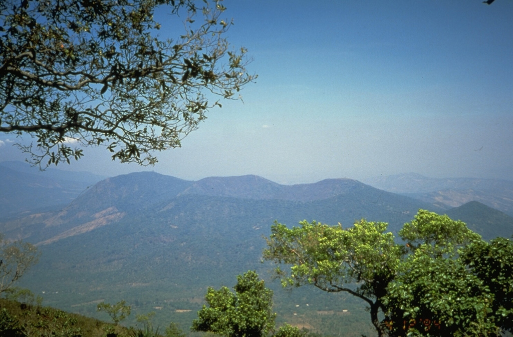 Chinameca is a small stratovolcano with a roughly 2-km-wide summit caldera, is seen here from San Miguel volcano to its SE. The Holocene Cerro el Limbo cone (left) is on the western flank, and a Holocene lava flow extends to the north from a vent on the NNW flank. The small peak on the far-right flank is Cerro Partido. Photo by Kristal Dorion, 1994 (U.S. Geological Survey).