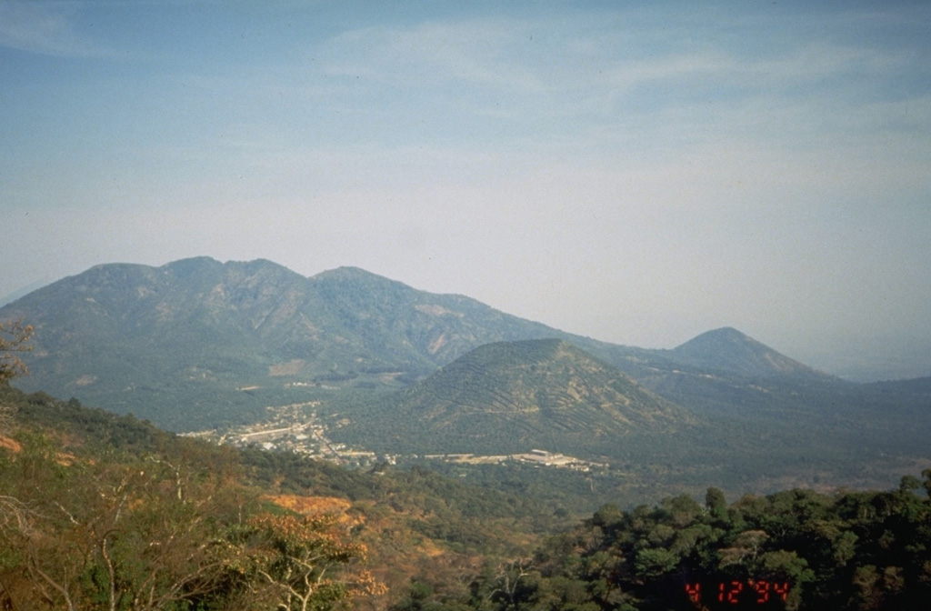 The eroded Pleistocene El Tigre volcano is seen here from the flank of Tecapa to the NW with the town of Santiago de María near the center. Two Holocene cones are seen here, Cerro Oromontique right of Santiago de María and Cerro la Manita, the small peak on the horizon to the right.  Photo by Kristal Dorion, 1994 (U.S. Geological Survey).