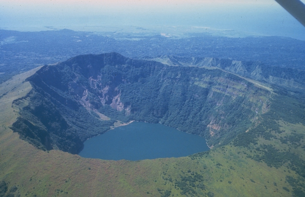 Cosigüina, seen here from the east, is a low basaltic-to-andesitic composite volcano that forms a large peninsula at the NW tip of Nicaragua along the Gulf of Fonseca.  The 872-m-high volcano has a pronounced somma rim, which forms the ridge seen here at the right behind the far crater rim.  The younger cone is truncated by a large elliptical prehistorical summit caldera 2 x 2.4 km in diameter and 500 m deep, which is now filled by a lake.  It was the source of a major explosive eruption in 1835, Nicaragua's largest during historical time.      Photo by Jaime Incer, 1981.