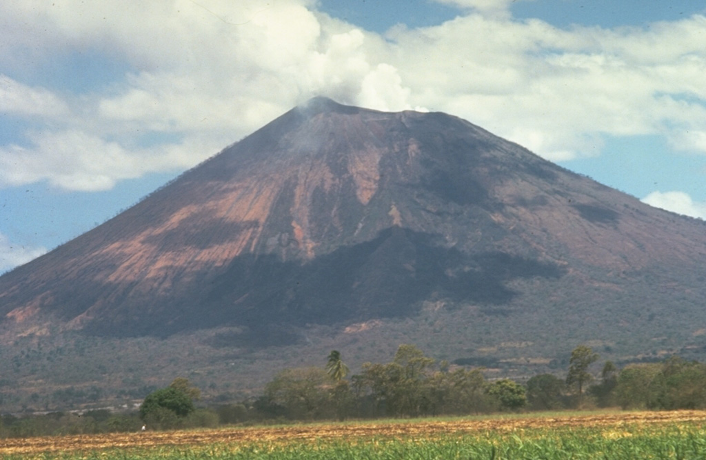 The San Cristóbal volcanic complex consists of five principal edifices.  The youngest cone, the namesake San Cristóbal, seen here from the south, is the highest peak of the Marrabios Range.  Several radial flank craters occur along a N-S line on the outer north flank of 1745-m-high San Cristóbal.  Historical activity, consisting of small-to-moderate explosive eruptions, has been reported since the 16th century.  The SW crater rim (left) rises 140 m above the NE rim because prevailing trade winds distribute tephra to the SW. Photo by Jaime Incer.