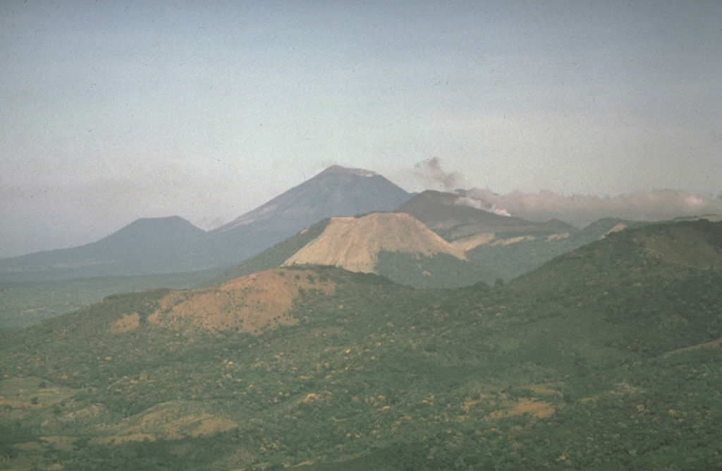 Cerro Negro volcano provides a vantage point for a NW-looking view down the Marrabios Range volcanic chain.  The forested slopes in the foreground are part of Rota volcano.  The light-colored conical peak in the center is Volcán Santa Clara, part of the Telica volcanic complex, whose principal peak, Telica itself, just pokes its head above the horizon behind and to the right of Santa Clara.  The large conical peak on the center horizon is San Cristóbal, the highest peak of the Marrabios Range.  The satellitic peak of El Chonco is on the left horizon. Photo by  Dennis Nielson, 1972 (courtesy of Mike Carr, Rutgers University).