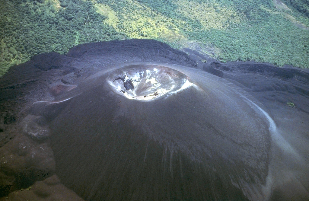 Cerro Negro, Central America's youngest volcano, is a pyroclastic cone that began growing in 1850.  It is seen here 130 years later in an aerial view from the NW.  The cone rises about 250 m above its base and is surrounded by lava flows that bank up against and are deflected by the slopes of Las Pilas volcano at the top of the photo.  More than 20 eruptions, separated by quiet intervals of a few years to a few decades, have taken place in the past century and a half at this small-volume basaltic volcano.   Photo by Jaime Incer, 1980.