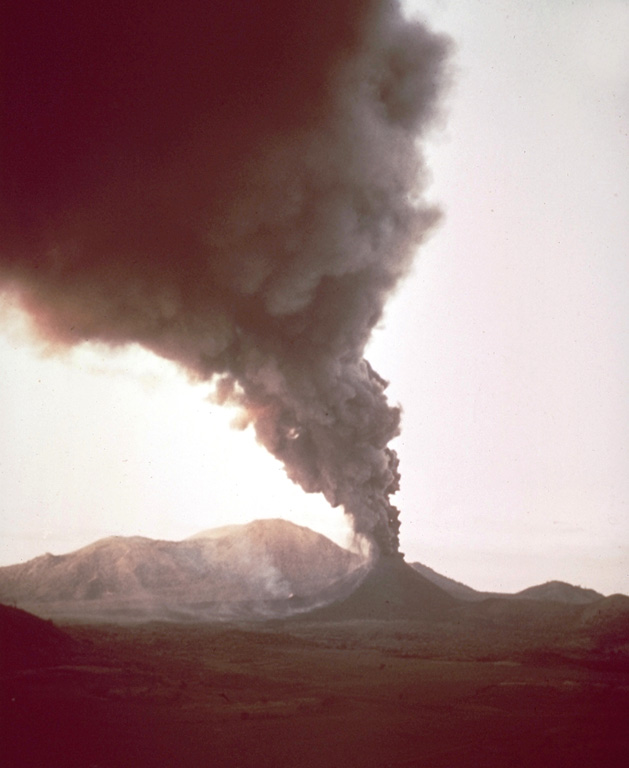 A dark ash-rich column rises above Cerro Negro volcano during the 1968 eruption.  The heavy ash cloud was distributed by prevailing winds to the west, darkening the sky in that direction while Las Pilas volcano in the background remains in the sunlight.  Ashfall damaged about 700 km2 of croplands. Photo by William Melson, 1968 (Smithsonian Institution).