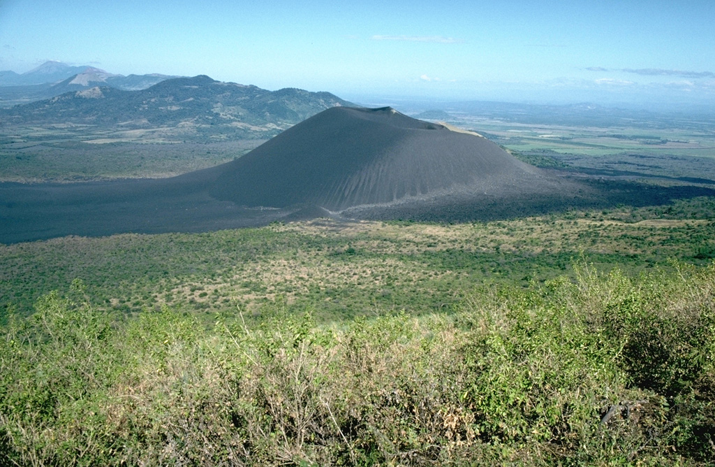 The unvegetated cone of Cerro Negro, the youngest volcano in Nicaragua, is seen here from the slopes of Las Pilas volcano at the end of its 1995 eruption.   Lava flows in 1995 traveled to the NNE (right).  Beyond Cerro Negro to the NW is the broad massif of Rota volcano.  Unlike Telica and San Cristóbal volcanoes in the distance at the far upper left, Rota has had no historical eruptions.   Photo by Britt Hill, 1995 (Southwest Research Institute).