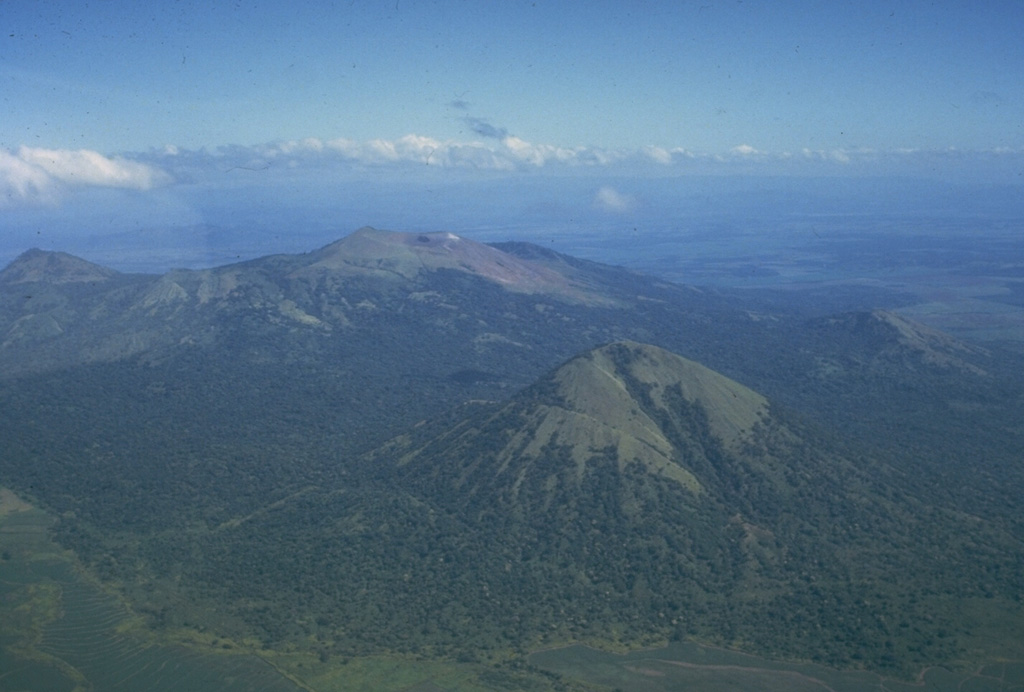 Las Pilas volcanic complex includes a cluster of cones, of which Las Pilas (El Hoyo), in the center background, is the largest.  A N-S fracture system cutting across the cone has produced numerous well-preserved flank vents, including maars.  Cerro Asososca is the prominent conical volcano in the right foreground of this photo from the SW.  Cerro Grande is the peak at the upper left.  The only certain historical eruptions of Las Pilas took place in the 1950s from a fissure that cut across the summit east of the 700-m-wide summit crater.    Photo by Jaime Incer, 1981