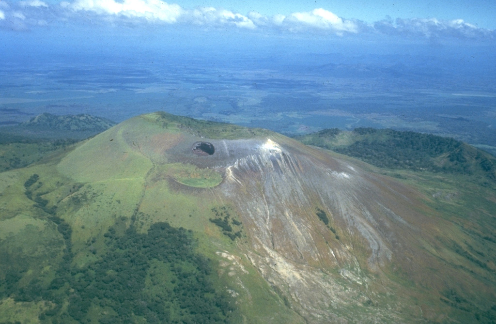 Las Pilas volcano is seen here in an aerial view from the south, with the dramatic El Hoyo pit crater below the summit at the left center.  The arcuate ridge at the right beyond Las Pilas is the NE rim of a large crater cutting the older Cerro el Picacho volcano.  The flat area in the background beyond Cerro el Picacho on the floor of the Nicaraguan depression is the Malpaisillo pyroclastic shield volcano.   Photo by Jaime Incer, 1981.