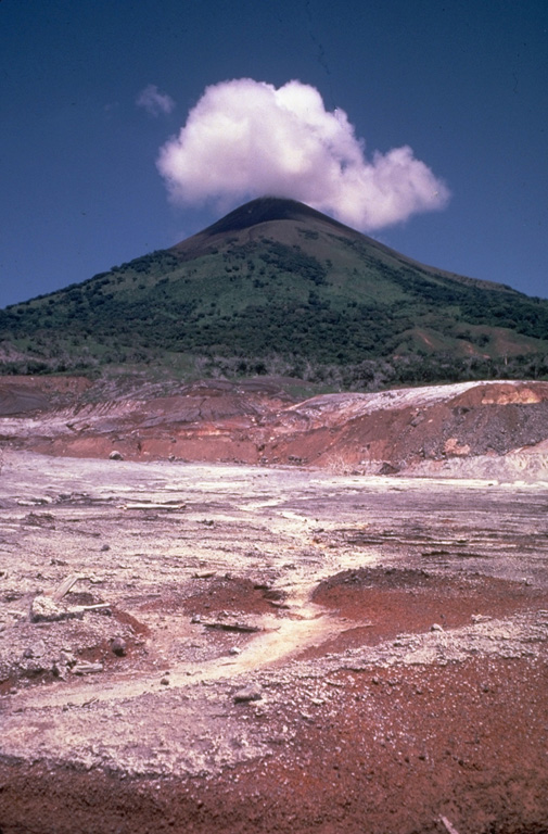 Hydrothermally altered ground in the foreground is part of 2 sq km geothermal field on the southern flank of Momotombo volcano.  The Patricio Arguello Ryan geothermal plant at one point produced 25% of the electrical power of Nicaragua.  Summit crater fumarolic activity increased following development of the geothermal field. Photo by Jaime Incer.